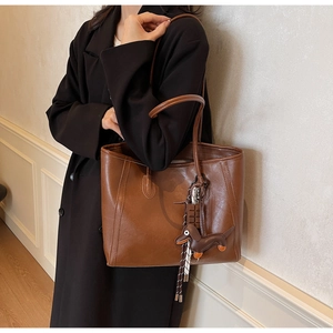 Close-up of brown vintage tote bag featuring dachshund charm and striped ribbon detail