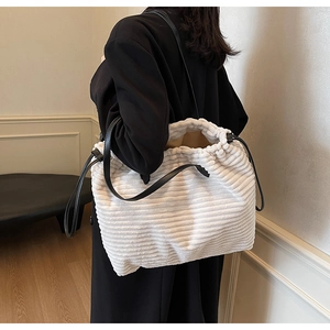 Close-up of a white corduroy tote bag with black leather straps on a model in a room