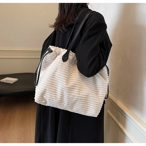 Detail of off-white corduroy tote bag with black leather straps on a model wearing a blazer