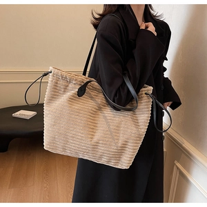 Close-up of beige corduroy tote bag showing vertical texture and black leather straps
