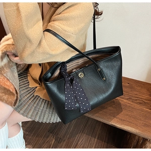 Close-up of black pebbled leather tote bag with gold logo and polka dot silk scarf