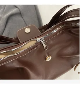 Detail of a dark brown leather tote featuring a silver zipper and white contrast stitching