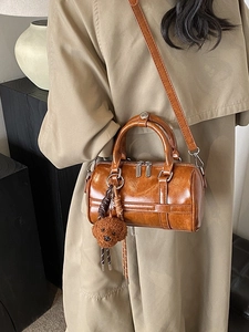 Sac Boston vintage marron avec breloque ours porté avec un trench-coat élégant