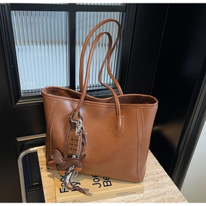 Detail of a brown leather tote bag with chocolate and dachshund pendants on a marble surface