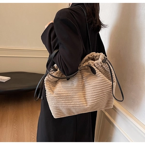 Detail of a large beige corduroy tote bag with drawstring closure and slim black leather strap