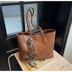 Brown vintage tote bag detail with chocolate and bird pendants on marble surface
