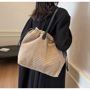 Detailed view of a beige corduroy tote bag worn over the shoulder with a black coat