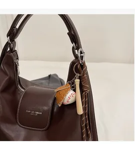 Detail of dark brown lychee leather tote bag with a baseball themed metal keychain