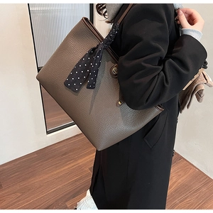 Detail of a brown leather tote bag with lychee texture and a polka dot silk scarf handle