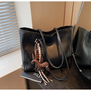 Close-up of black matte tote bag with leather puppy charm and woven rope detail