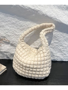 Bolso bombonera acolchado blanco crema con textura de nube y asa sobre base de piedra