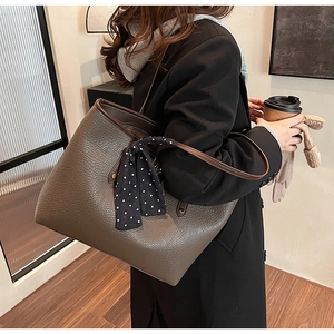 Side view of a large brown tote bag with pebble leather texture and a polka dot scarf handle