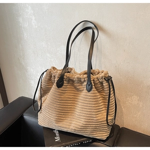 Detail of khaki corduroy tote bag with black leather drawstrings on a leather bench