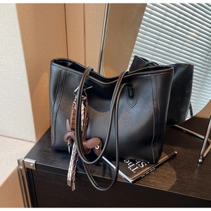 Detail of black pebbled leather tote bag with thin straps and a cute dog bag charm