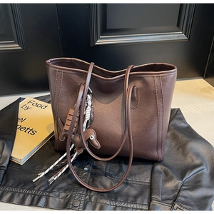 Detail of dark brown faux leather tote bag with animal charm on a leather jacket