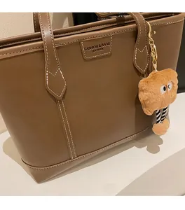 Détail du sac cabas en cuir marron foncé avec logo cousu et breloque peluche jaune
