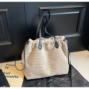 Detail of beige corduroy tote bag with drawstring closure and black leather handles