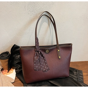 Detail of dark red lychee grain leather tote bag with gold logo and polka dot silk scarf