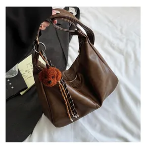 Detail view of a dark brown hobo shoulder bag featuring a plush orange bear pendant