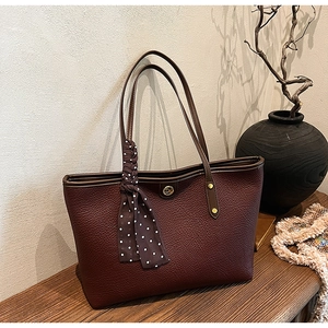 Close-up of wine red lychee leather tote bag with polka dot scarf and gold logo