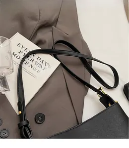 Détail d'une bandoulière en cuir réglable avec boucle en métal doré sur un sac seau noir
