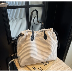 Detail of corduroy tote bag featuring cream fabric texture and black leather shoulder strap