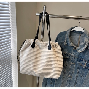 Detail of beige corduroy tote bag with textured horizontal stripes and black leather handles