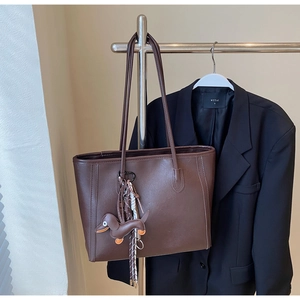 Detailed macro view of dark brown faux leather tote with dachshund charm and woven strap