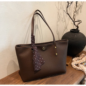 Close-up of deep brown lychee grain leather tote bag with silk scarf and gold logo