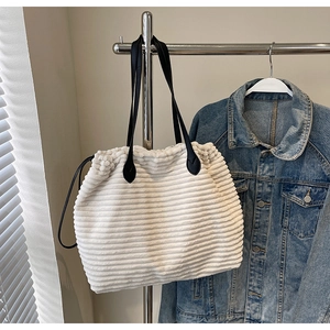 Detail of white corduroy tote bag with black leather straps and drawstring closure