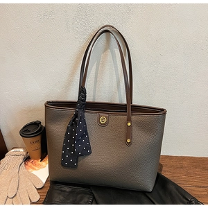 Detail of dark brown pebble leather tote bag with gold DM logo and polka dot silk scarf