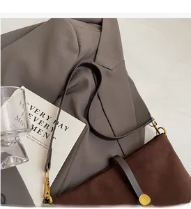 Close-up of dark brown suede shoulder bag featuring a round golden metallic clasp detail