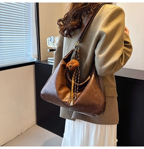 Detail of a large dark brown hobo bag with a plush bear pendant on a model in a suit