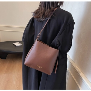 Sac seau en cuir marron porté en bandoulière par un mannequin en intérieur