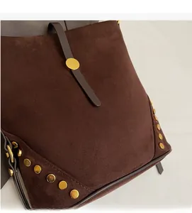 Detail shot of brown suede bucket bag featuring golden rivets and smooth leather straps