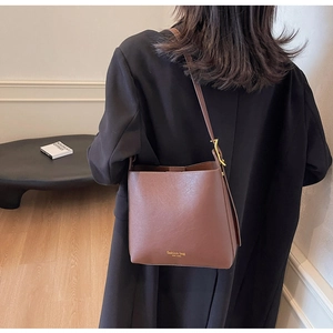 Détail d'un sac seau marron avec texture lychee et bandoulière réglable à boucle d'or