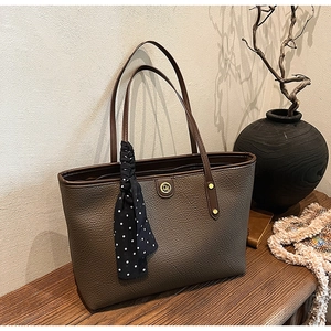 Detail of dark brown leather tote bag with polka dot scarf on a wooden surface