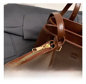 Detail of premium brown leather tote featuring gold metal zipper and embossed side logo