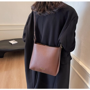 Sac seau en cuir marron avec large bandoulière porté par un mannequin en manteau noir