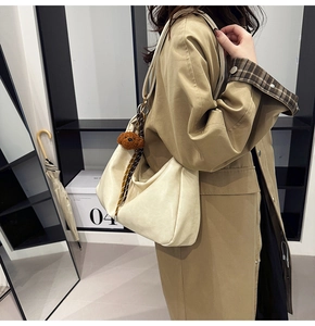 Chic cream hobo bag shown on shoulder with a cute brown plush bear charm detail