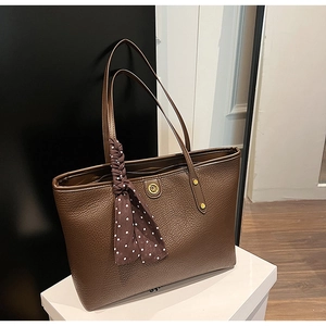 Close-up of brown litchi leather tote bag with gold logo and polka dot silk scarf