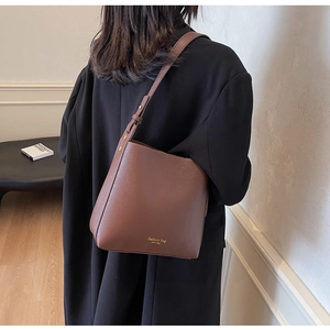 Détail d'un sac seau en cuir marron avec bandoulière réglable et lettrage doré élégant