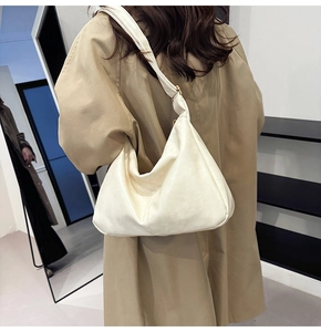 Detail of a white pleated half-moon shoulder bag with adjustable strap on a beige coat