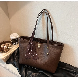 Close-up of brown pebbled leather tote bag featuring a decorative silk scarf and logo