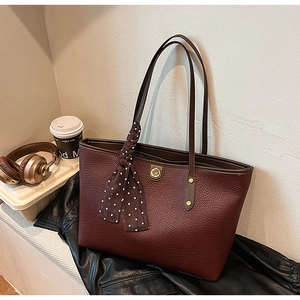 Close-up of a burgundy leather tote bag with a polka dot scarf and golden logo