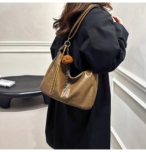 Detail of a brown PU leather hobo bag featuring a plush teddy bear and woven tassel charm