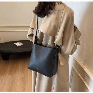 Vue latérale d'un sac seau en cuir noir avec large bandoulière porté par un mannequin