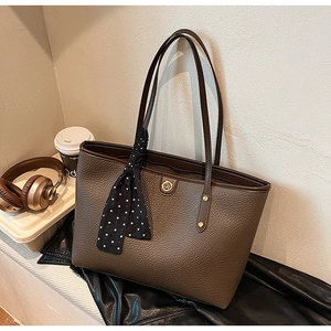 Detail of dark brown pebble leather tote with gold logo and polka dot silk scarf