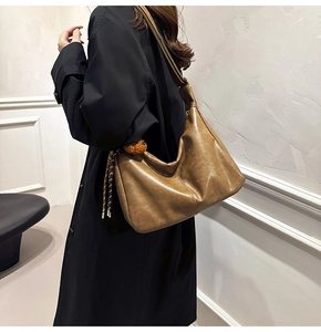 Detailed side view of a large brown hobo bag featuring a fuzzy ball charm accent