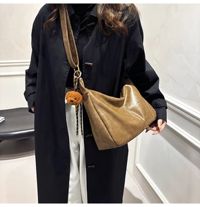 Brown vintage faux leather hobo bag with plush bear charm worn by a model in a coat